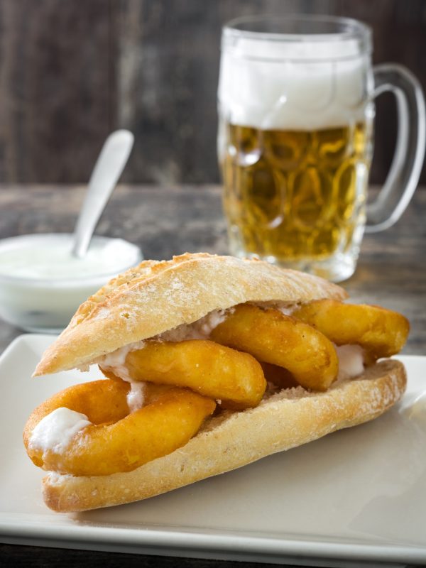 Bocadillo de calamares and beer resting on wooden table